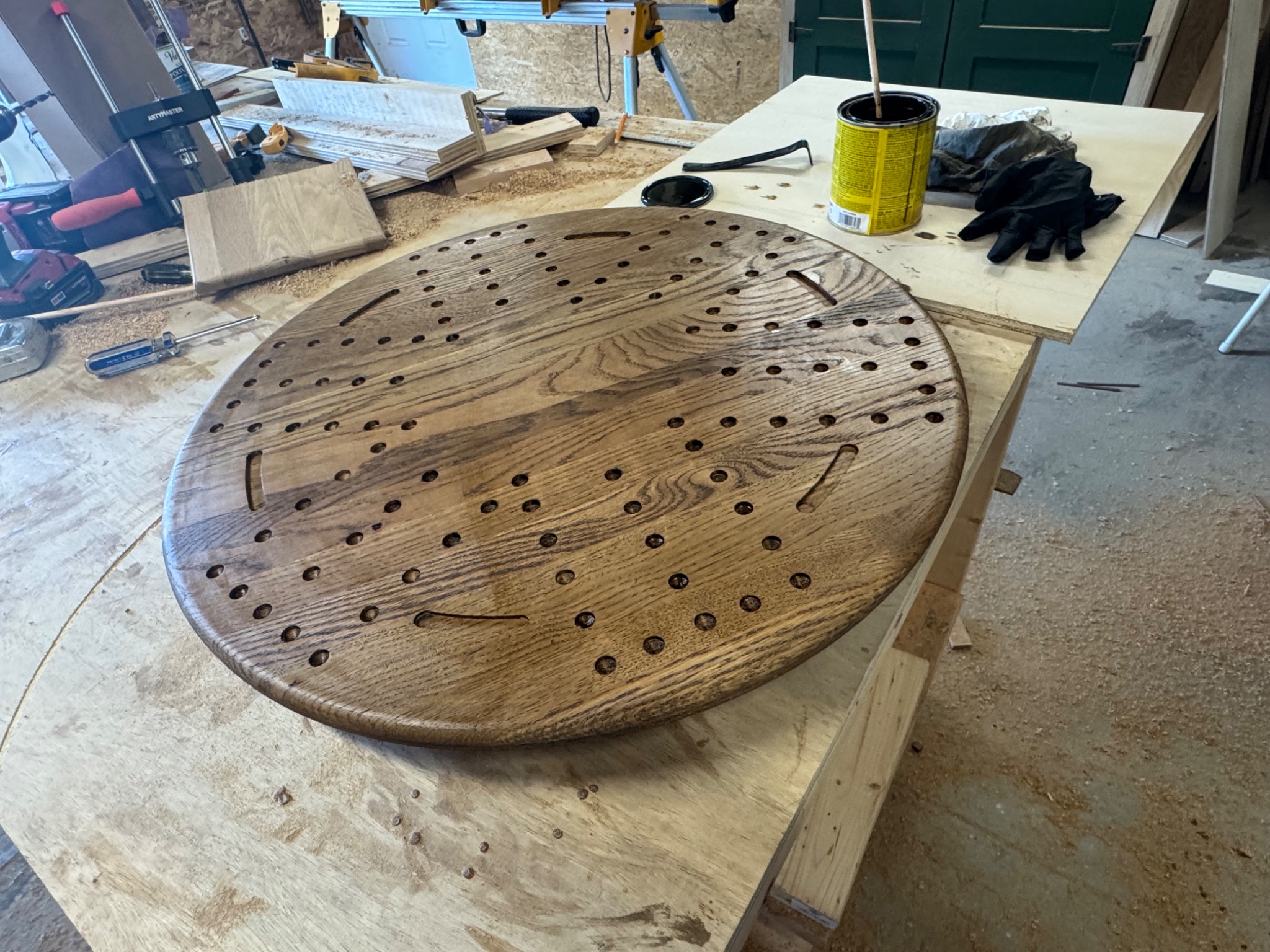 Round wooden cribbage board and matching small wooden box on a workshop bench