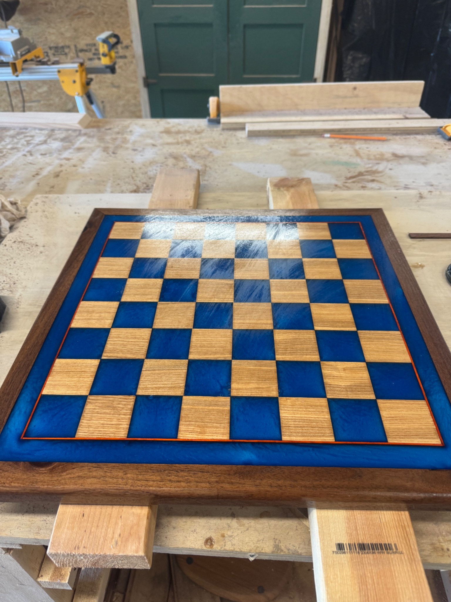 Blue epoxy and natural wood chessboard photographed on a woodworking bench